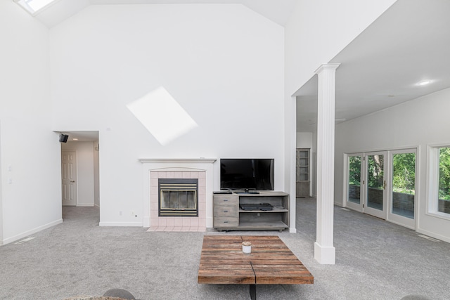 unfurnished living room featuring a tile fireplace, light carpet, high vaulted ceiling, and ornate columns