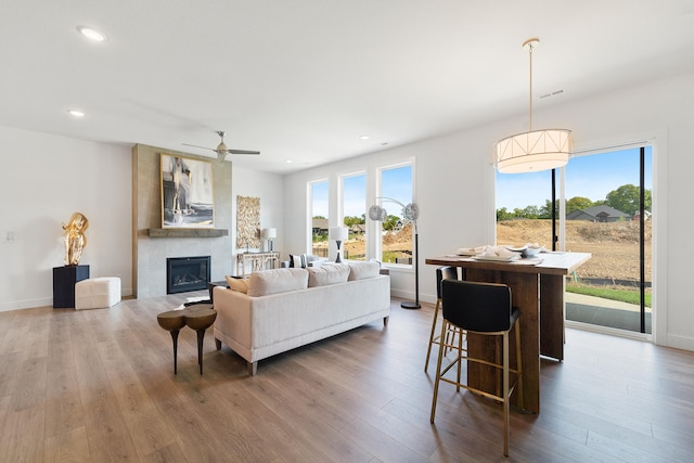 living room featuring ceiling fan, a large fireplace, and dark wood-type flooring