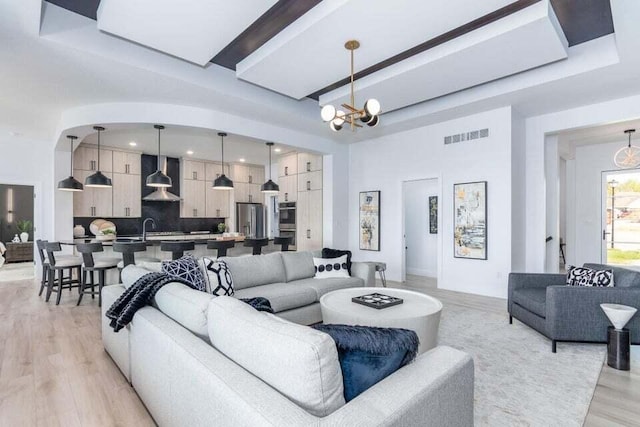 living room featuring beam ceiling, an inviting chandelier, light hardwood / wood-style floors, and sink