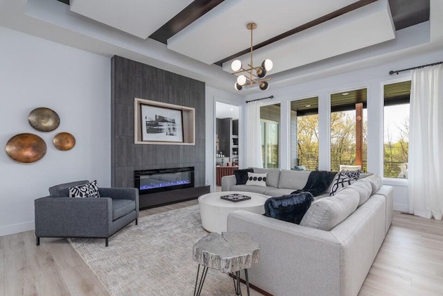 living room featuring beamed ceiling, light hardwood / wood-style floors, a large fireplace, and an inviting chandelier