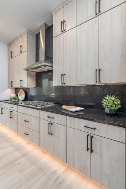 kitchen with light wood-type flooring, tasteful backsplash, wall chimney range hood, dark stone countertops, and stainless steel gas stovetop