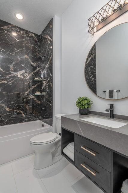 full bathroom with tile flooring, large vanity, toilet, and tiled shower / bath