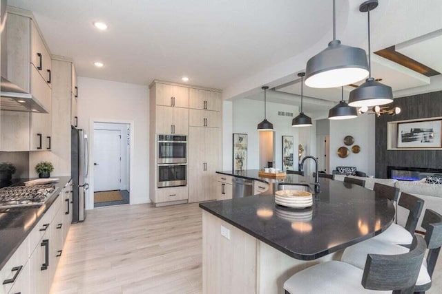 kitchen featuring a breakfast bar area, stainless steel appliances, light hardwood / wood-style flooring, pendant lighting, and sink