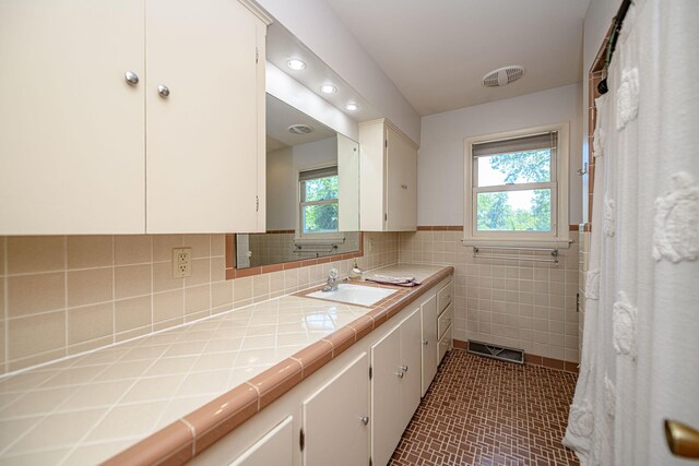 full bath with healthy amount of natural light, tile walls, vanity, tile patterned flooring, and wainscoting