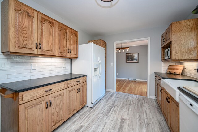 kitchen with white appliances, backsplash, light wood finished floors, dark countertops, and a chandelier