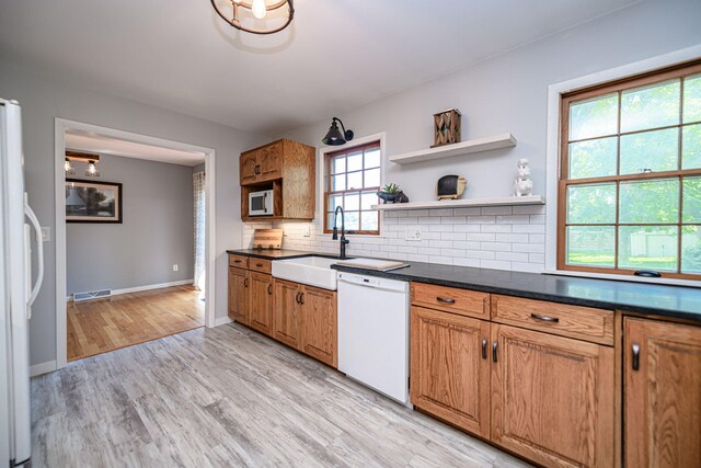 kitchen featuring white appliances, a sink, decorative backsplash, light wood-type flooring, and baseboards