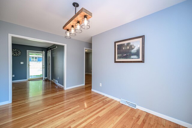 unfurnished room featuring light wood-style flooring, baseboards, and a chandelier