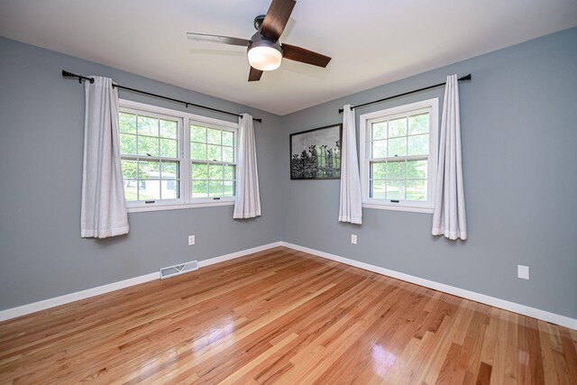 empty room with plenty of natural light, wood finished floors, ceiling fan, and baseboards
