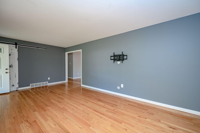 unfurnished room featuring light wood-style flooring, baseboards, and a barn door