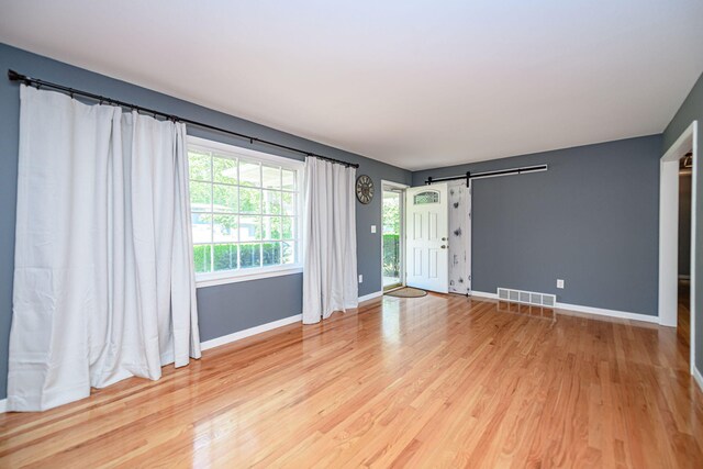 unfurnished living room with a barn door, light wood finished floors, and baseboards