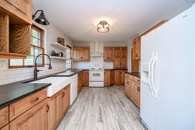 kitchen featuring white appliances, wall chimney range hood, dark countertops, a sink, and backsplash