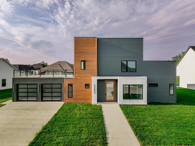 contemporary home featuring driveway, a front lawn, an attached garage, and a balcony