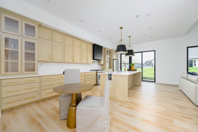 kitchen featuring light hardwood / wood-style flooring, backsplash, light brown cabinetry, and a center island with sink