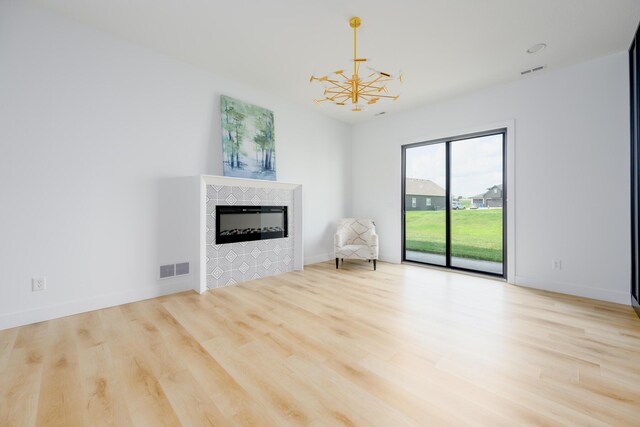 unfurnished room with a chandelier, a tiled fireplace, wood finished floors, and visible vents