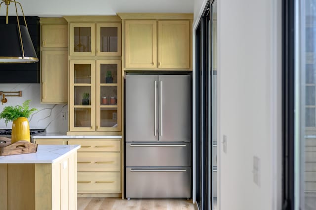 kitchen with glass insert cabinets, freestanding refrigerator, light countertops, and decorative backsplash