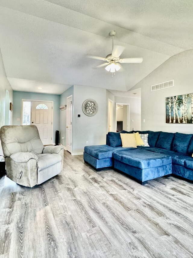 living room featuring vaulted ceiling, ceiling fan, light hardwood / wood-style floors, and a textured ceiling