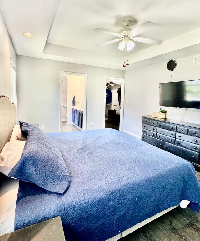 bedroom with ensuite bath, ceiling fan, dark hardwood / wood-style floors, a walk in closet, and a raised ceiling