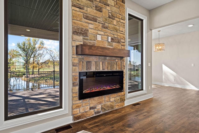 unfurnished living room with a notable chandelier, a stone fireplace, and dark wood-type flooring