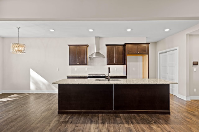 kitchen featuring wall chimney range hood, dark hardwood / wood-style flooring, a kitchen island with sink, and sink