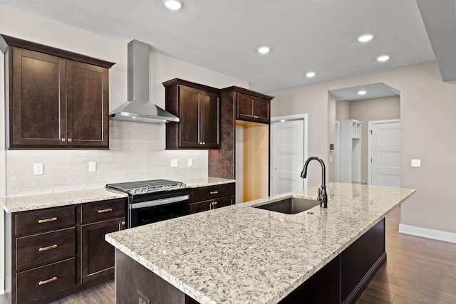 kitchen featuring sink, stainless steel gas range oven, light stone countertops, wall chimney exhaust hood, and tasteful backsplash