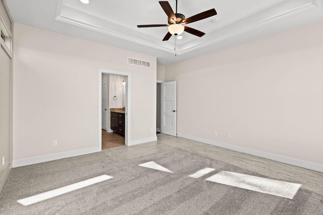 unfurnished bedroom featuring ceiling fan, ensuite bathroom, light carpet, and a tray ceiling