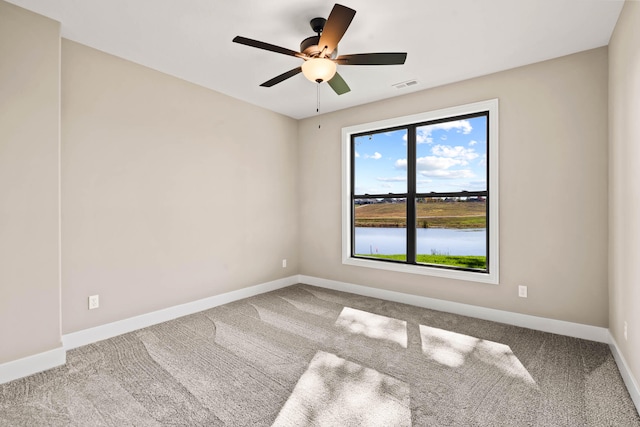 carpeted spare room featuring ceiling fan and a water view