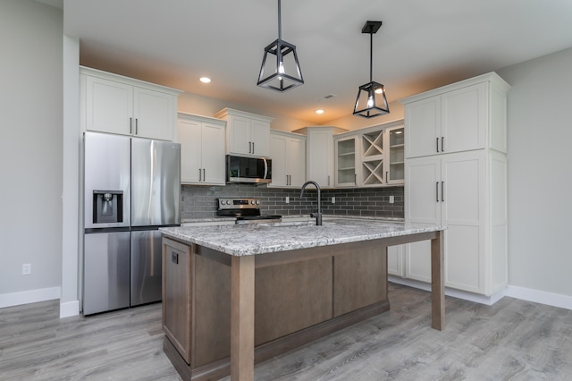 kitchen featuring stainless steel appliances, light hardwood / wood-style floors, light stone counters, white cabinets, and pendant lighting