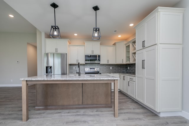 kitchen with a kitchen island with sink, appliances with stainless steel finishes, decorative light fixtures, and light stone counters