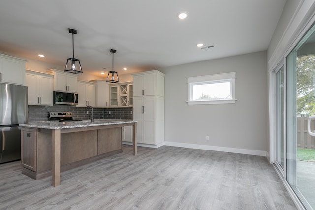 kitchen with white cabinetry, appliances with stainless steel finishes, pendant lighting, light stone countertops, and a kitchen island with sink