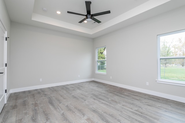 unfurnished room featuring light wood-type flooring, a healthy amount of sunlight, ceiling fan, and a tray ceiling