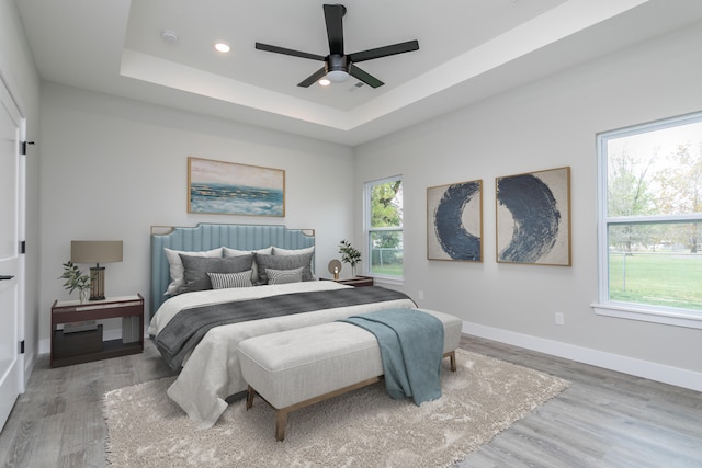 bedroom with a tray ceiling, multiple windows, wood-type flooring, and ceiling fan