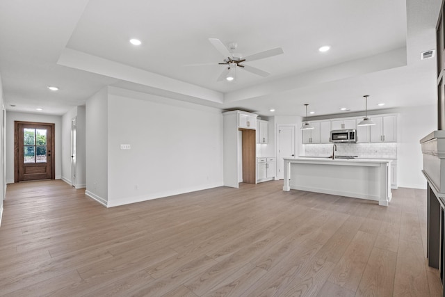 unfurnished living room with light wood-type flooring, a raised ceiling, ceiling fan, and sink