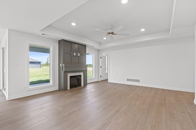 unfurnished living room featuring a fireplace, a raised ceiling, and light hardwood / wood-style flooring