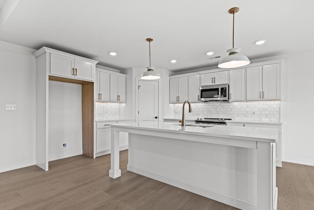 kitchen featuring sink, hanging light fixtures, light hardwood / wood-style floors, a center island with sink, and white cabinets