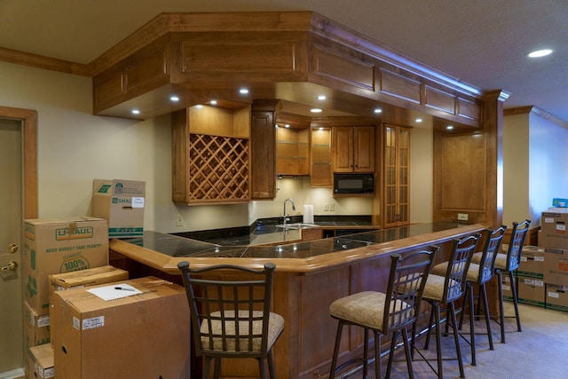 kitchen featuring carpet, black microwave, crown molding, kitchen peninsula, and a kitchen breakfast bar