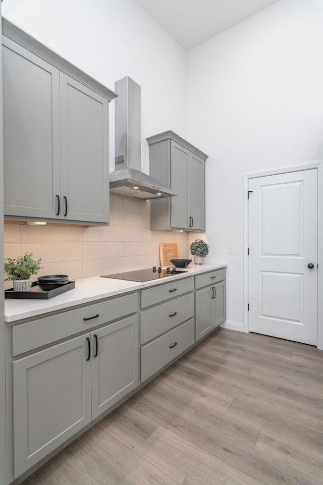 kitchen featuring black electric cooktop, gray cabinetry, light hardwood / wood-style floors, and wall chimney range hood