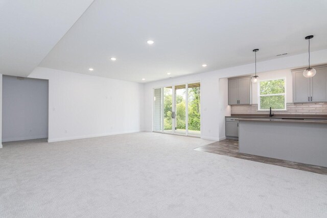 unfurnished living room featuring a wealth of natural light, sink, and light colored carpet