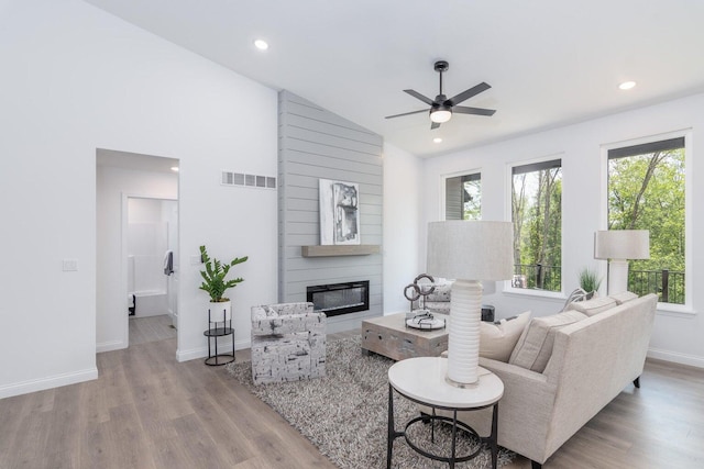 living room with ceiling fan, light wood-type flooring, a fireplace, and vaulted ceiling