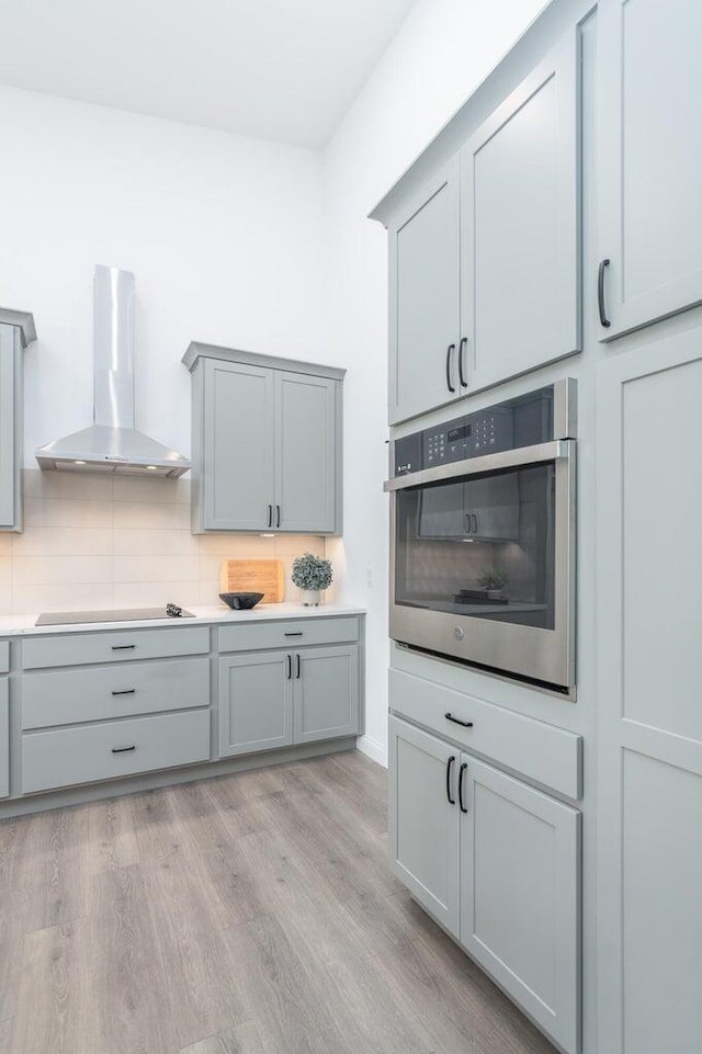 kitchen featuring gray cabinets, wall chimney exhaust hood, oven, and light hardwood / wood-style floors