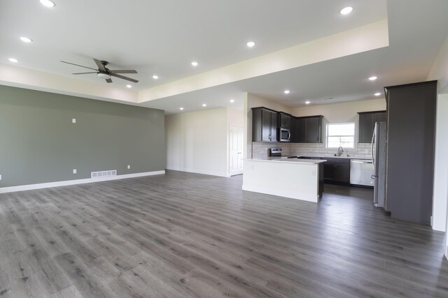 unfurnished living room with sink, a tray ceiling, dark hardwood / wood-style floors, and ceiling fan