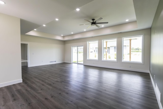 empty room with baseboards, visible vents, a tray ceiling, ceiling fan, and dark wood-type flooring