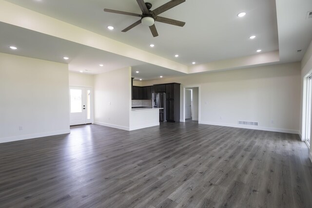 unfurnished living room featuring ceiling fan, a tray ceiling, and dark hardwood / wood-style flooring