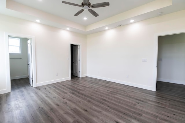 unfurnished bedroom featuring dark wood-type flooring, a walk in closet, and a tray ceiling