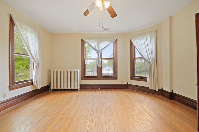 spare room featuring light hardwood / wood-style flooring, a wealth of natural light, ceiling fan, and radiator