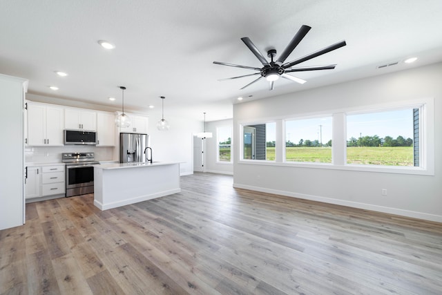 kitchen featuring appliances with stainless steel finishes, white cabinets, hanging light fixtures, a kitchen island with sink, and light hardwood / wood-style flooring