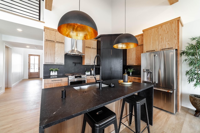 kitchen with wall chimney exhaust hood, stainless steel appliances, backsplash, and light wood-type flooring