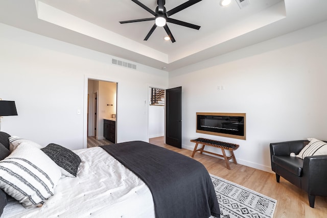 bedroom featuring ceiling fan, connected bathroom, a tray ceiling, and light hardwood / wood-style floors