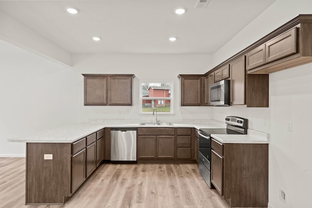 kitchen with light stone countertops, sink, stainless steel appliances, kitchen peninsula, and light hardwood / wood-style floors