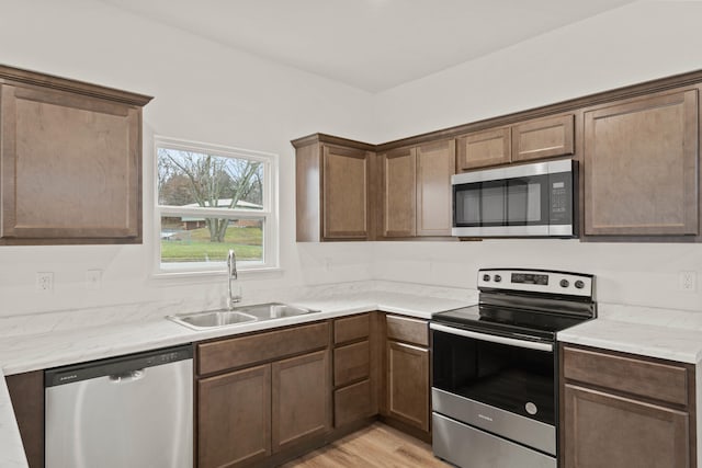 kitchen featuring light hardwood / wood-style floors, light stone countertops, sink, and appliances with stainless steel finishes