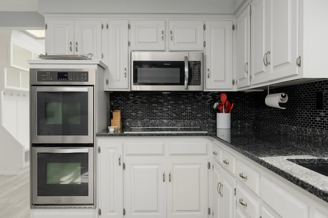 kitchen with dark stone countertops, light hardwood / wood-style flooring, stainless steel appliances, white cabinets, and backsplash